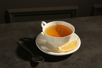 Refreshing green tea in cup, slice of lemon and spoon on dark textured table