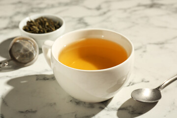 Refreshing green tea in cup and spoon on white marble table, closeup