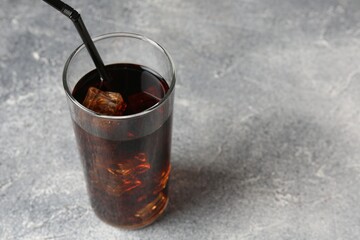 Refreshing cola with ice cubes and drinking straw in glass on light textured table, closeup. Space for text