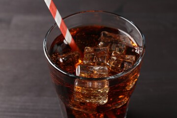 Refreshing cola with ice cubes and drinking straw in glass on black wooden table, closeup