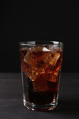 Refreshing cola with ice cubes in glass on black wooden table, closeup