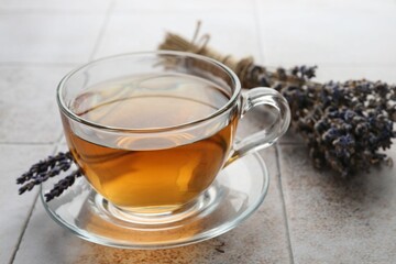 Aromatic lavender tea in glass cup and dry flowers on white tiled table, closeup