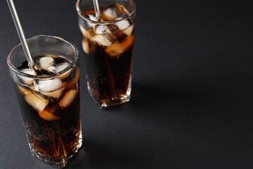 Refreshing cola with ice cubes and drinking straws in glasses on black table, closeup. Space for text