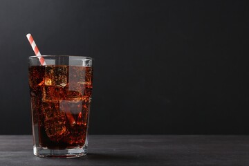 Refreshing cola with ice cubes and drinking straw in glass on black wooden table, closeup. Space for text