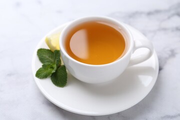 Aromatic mint tea in cup, fresh leaves and lemon on light marble table, closeup