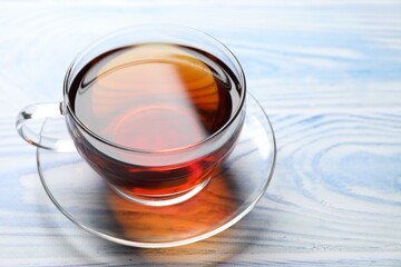 Aromatic black tea in cup on light blue wooden table, closeup. Space for text