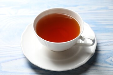 Aromatic black tea in cup on light blue wooden table, closeup