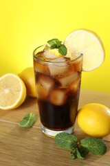 Refreshing iced cola with mint and lemons on wooden table