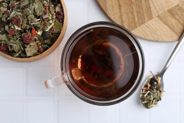 Delicious herbal tea and dry leaves on white tiled table, flat lay
