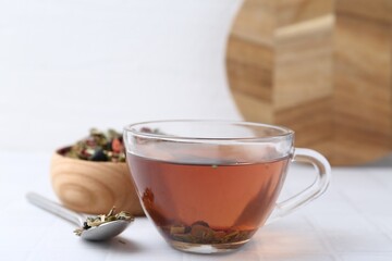 Delicious herbal tea and dry leaves on white tiled table, closeup