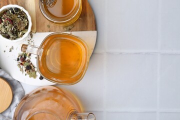 Delicious herbal tea with honey and dry leaves on white tiled table, flat lay. Space for text