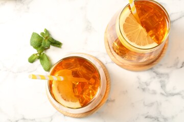 Refreshing iced tea with slices of lemon, mint and drinking straws on white marble table, flat lay