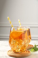 Refreshing iced tea with slices of lemon and drinking straws on white marble table, closeup