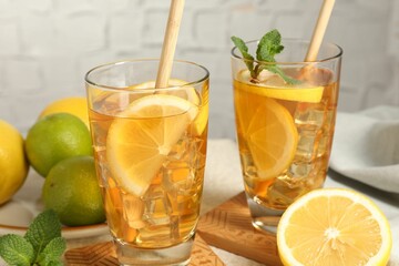 Refreshing iced tea with drinking straws, mint, lemon and lime on light table against grey background, closeup