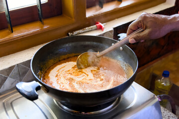 Cooking Indian Curry in a Pan with a Ladle on a Stove Near a Window