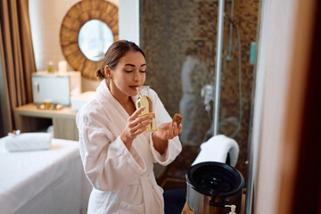 Young woman smelling aromatherapy oil with her eyes closed at spa.
