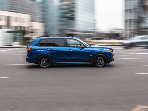 BMW X7 M60i car driving in city with motion blur, view from the side