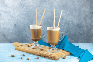 Two glasses of almond coffee resting on wooden board with scattered almonds