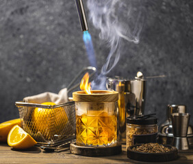 Bartender using torch to prepare smoked cocktail with orange