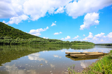 Old wooden fishing boats anchored along the riverbank on a sunny day. Beautiful sky with white...