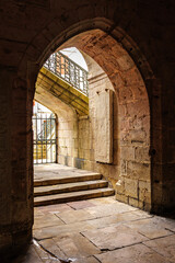 Arched stone passage leading to the entrance of Saint-Jean-Baptiste Church in Saint-Jean-de-Luz, France, featuring a historical stone slab and an ornate staircase with wrought iron railing.