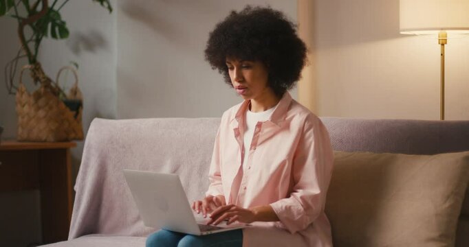 Hispanic woman copywriter types on laptop sitting on sofa