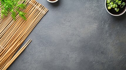 A top-down view of a grey table displays arranged bamboo rolling mat on one side and chopsticks on the other. There is ample negative space above for text or design. 