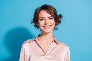 Charming businesswoman in a satin blouse smiles against a vibrant blue backdrop capturing elegance...