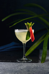 Refreshing yellow cocktail decorated with chili pepper and mint in elegant coupe glass