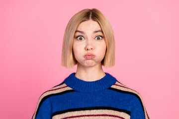 Funny woman puffing her cheeks in a trendy striped sweater against a pink background