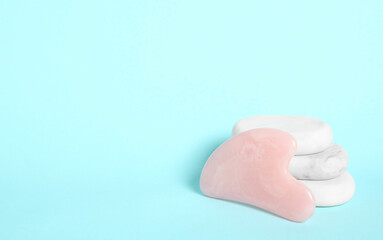 Rose quartz gua sha tool and spa stones on light blue background. Space for text
