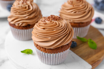 Tasty cupcakes with chocolate cream and blueberries on white marble table, closeup