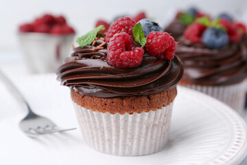 Tasty cupcakes with chocolate cream and berries on table, closeup