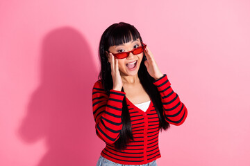 Energetic young woman wearing a striped cardigan expresses joy with playful gestures against a...