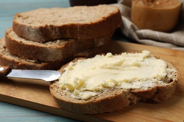 Fresh bread with butter and knife on blue wooden table, closeup