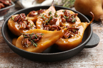 Delicious pears with caramel sauce, pecan nuts and thyme on wooden table, closeup