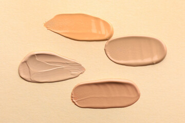 Samples of different foundations on beige background, top view