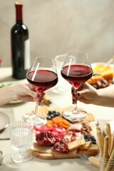 Women clinking glasses of wine during dinner at table indoors, closeup