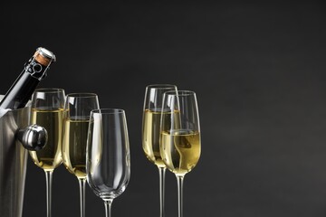 Bottle of sparkling wine in cooler bucket and glasses against grey background, closeup. Space for text