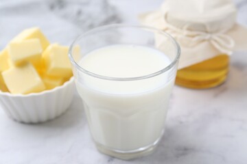 Fresh milk in glass, honey and butter on white marble table, closeup