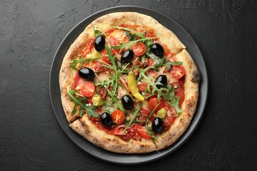 Tasty pizza with tomatoes, olives, chili and arugula on black table, top view