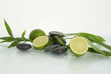 Spa composition with limes, massage stones and bamboo stem on wet surface against white background