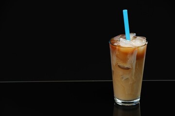 Refreshing iced coffee with milk in glass on black mirror surface. Space for text