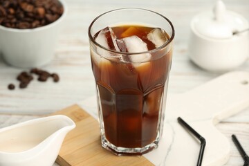 Refreshing iced coffee in glass and beans on white wooden table, closeup