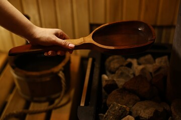 Woman pouring water on stones in sauna, closeup