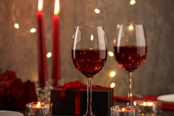 Glasses of wine, burning candles, gift box and roses on table, closeup. Romantic dinner