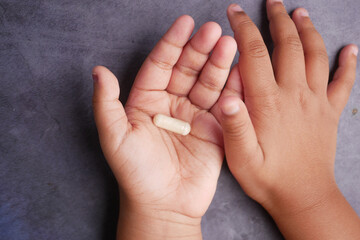 Hands of a child holding a capsule on a table