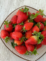 A bowl of fresh, vibrant strawberries on a textured wooden surface, highlighting their natural red color and appetizing appeal