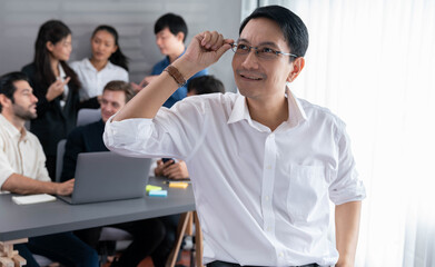 Confidence and happy smiling businessman portrait with background of his colleague and business team working in office. Office worker teamwork and positive workplace concept. Prudent