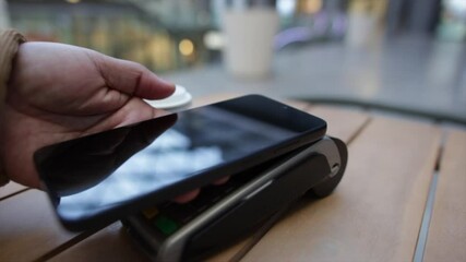 Wireless digital payment featuring smartphone touching payment terminal, processing cashless transaction near takeaway coffee cup inside modern cafe environment